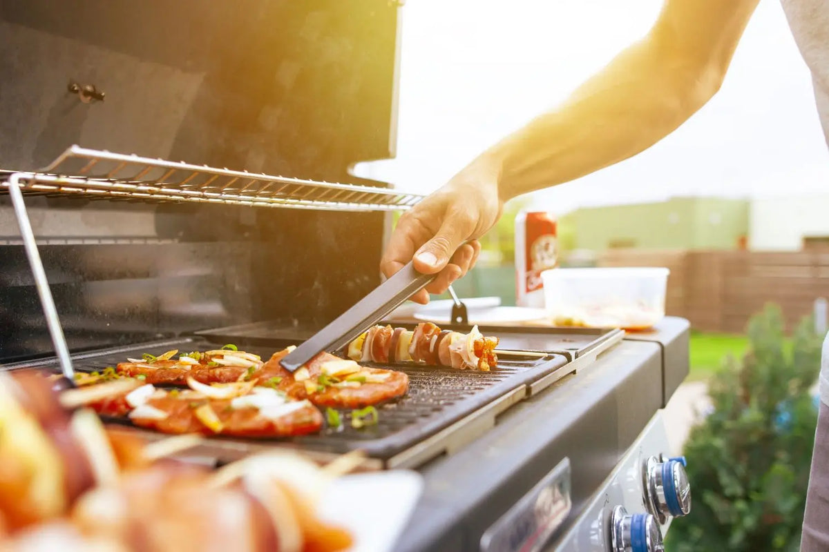 Backyard gas grill with stainless steel body and side burners, cooking food over an open flame